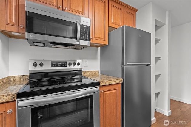 kitchen featuring baseboards, light stone countertops, appliances with stainless steel finishes, wood finished floors, and brown cabinetry