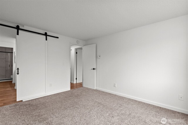 unfurnished bedroom with baseboards, carpet floors, a textured ceiling, a barn door, and baseboard heating