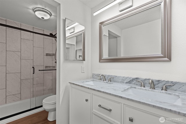 full bathroom featuring a sink, toilet, wood finished floors, and a shower stall