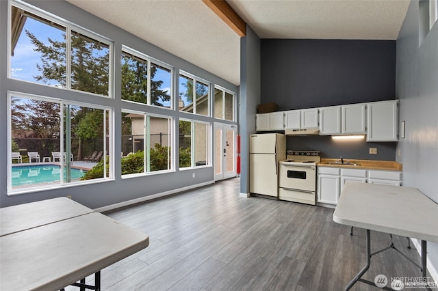 kitchen with a towering ceiling, wood finished floors, white appliances, white cabinetry, and a sink