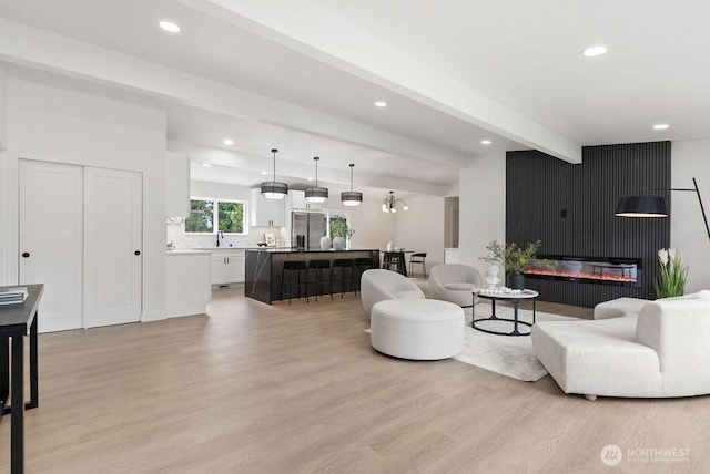 living room featuring light wood finished floors, beamed ceiling, recessed lighting, and a glass covered fireplace