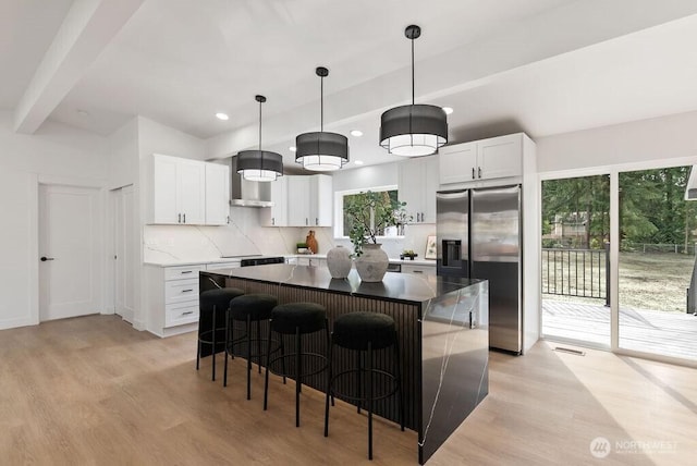 kitchen with a kitchen island, decorative backsplash, stainless steel refrigerator with ice dispenser, wall chimney exhaust hood, and light wood-type flooring