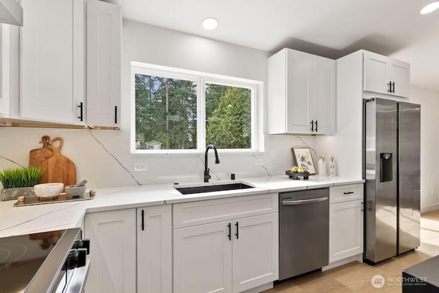 kitchen with light stone countertops, appliances with stainless steel finishes, white cabinetry, and a sink