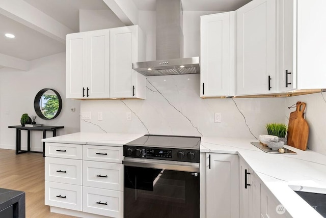 kitchen with electric range, light stone counters, tasteful backsplash, wall chimney exhaust hood, and white cabinets