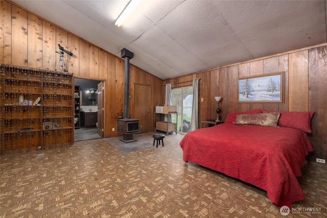 bedroom featuring vaulted ceiling, wood walls, a wood stove, and ensuite bathroom