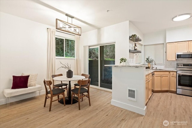 kitchen featuring light brown cabinets, decorative backsplash, appliances with stainless steel finishes, and light wood-type flooring