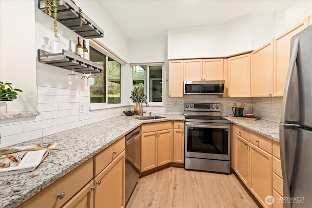 kitchen featuring light brown cabinetry, stainless steel appliances, light wood-style floors, and a sink