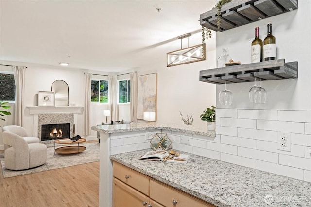 kitchen featuring light wood-style flooring, backsplash, a glass covered fireplace, open floor plan, and light stone countertops