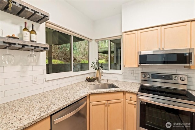 kitchen featuring light stone countertops, light brown cabinetry, decorative backsplash, a sink, and appliances with stainless steel finishes