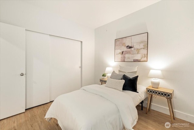 bedroom with light wood-style flooring, baseboards, and a closet