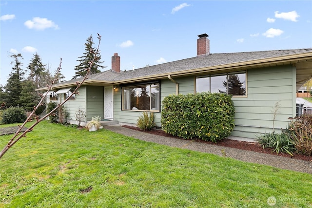 back of property with a shingled roof, a yard, and a chimney