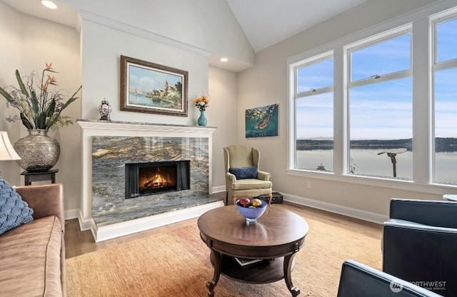 living area with baseboards, a water view, lofted ceiling, a fireplace, and wood finished floors