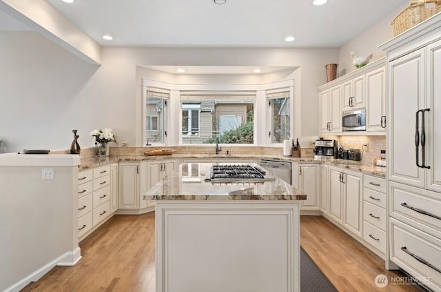 kitchen with appliances with stainless steel finishes, a center island, light wood-style floors, and light stone countertops