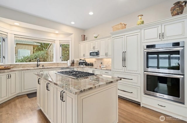 kitchen with light stone counters, a kitchen island, appliances with stainless steel finishes, and light wood-style flooring