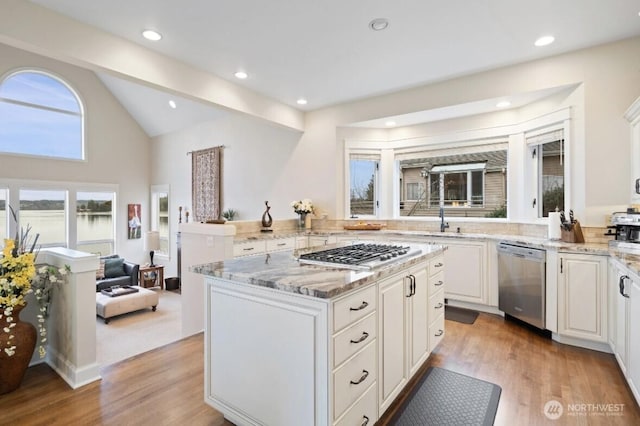 kitchen featuring stainless steel appliances, light stone countertops, light wood-style floors, and vaulted ceiling