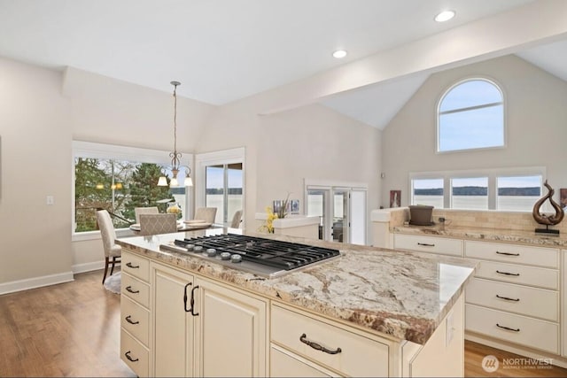 kitchen with light stone counters, stainless steel gas stovetop, a healthy amount of sunlight, and vaulted ceiling