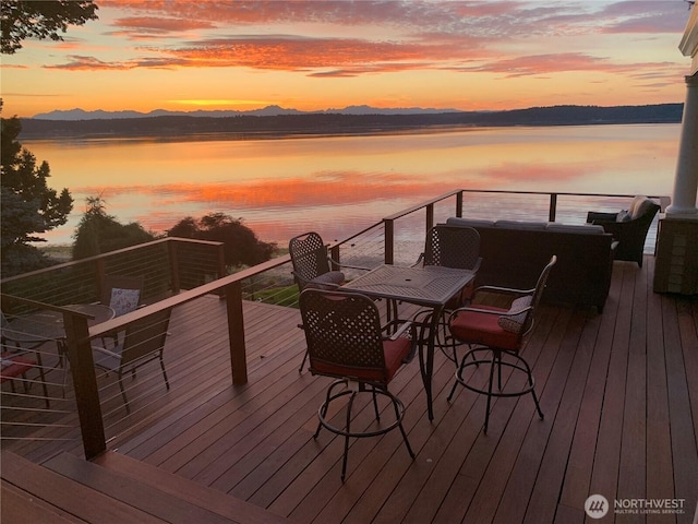 deck at dusk featuring a water and mountain view