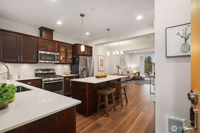 kitchen featuring a breakfast bar area, a sink, dark brown cabinetry, appliances with stainless steel finishes, and a center island