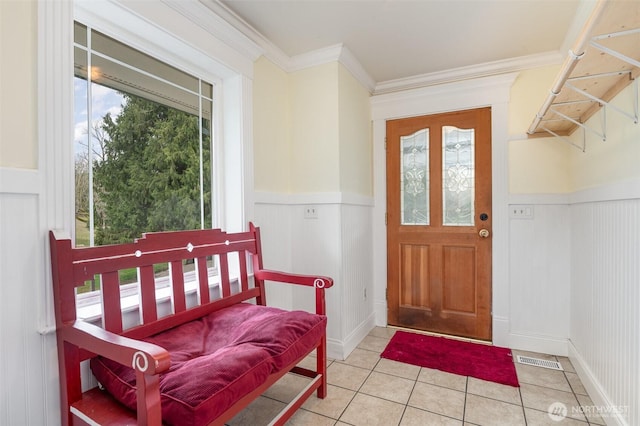 entryway with light tile patterned floors, a wainscoted wall, and ornamental molding