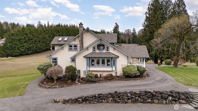 view of front facade with driveway, a chimney, a front yard, and a shingled roof