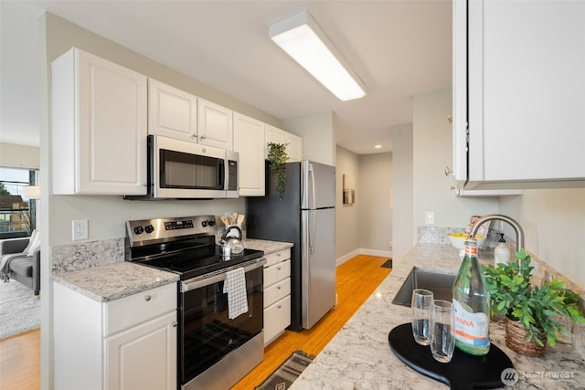 kitchen featuring light wood finished floors, light stone countertops, appliances with stainless steel finishes, white cabinets, and a sink