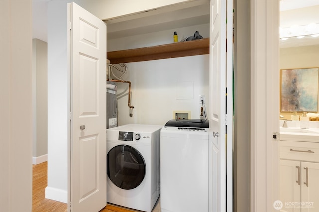 clothes washing area with baseboards, laundry area, a sink, light wood-style floors, and washing machine and dryer