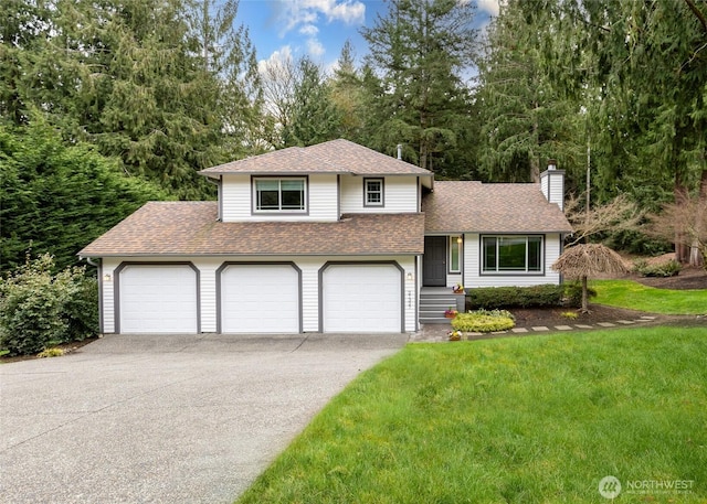 split level home featuring a front yard, driveway, roof with shingles, a chimney, and a garage