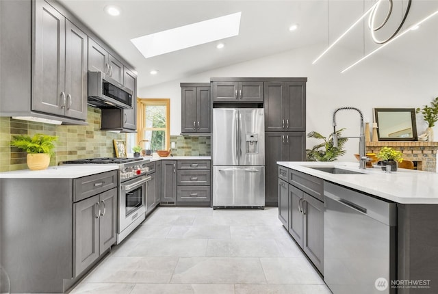 kitchen with light countertops, vaulted ceiling with skylight, gray cabinets, stainless steel appliances, and a sink