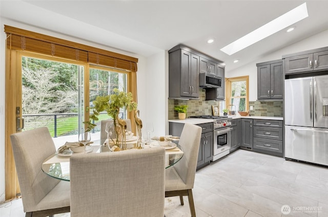 kitchen featuring lofted ceiling with skylight, gray cabinets, stainless steel appliances, light countertops, and decorative backsplash