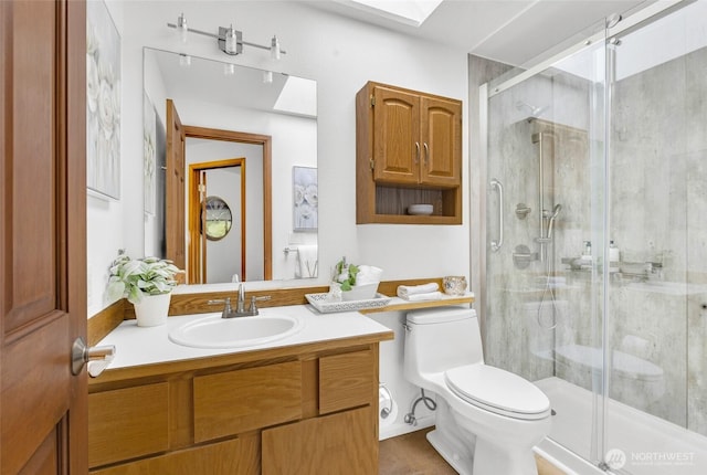 bathroom featuring toilet, a stall shower, a skylight, and vanity