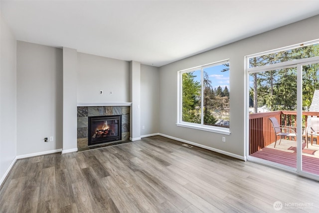 unfurnished living room featuring visible vents, baseboards, wood finished floors, and a tiled fireplace