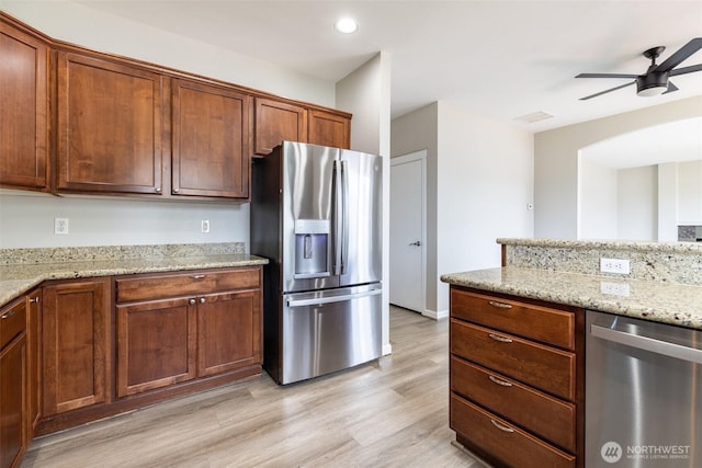 kitchen featuring light stone counters, a ceiling fan, light wood finished floors, and stainless steel appliances