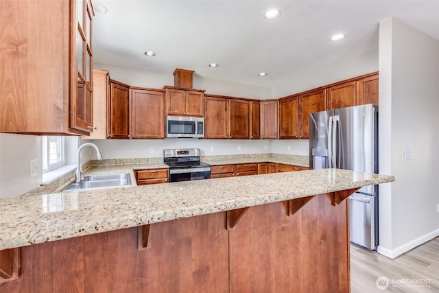 kitchen with light wood-style flooring, a sink, light stone counters, stainless steel appliances, and a peninsula