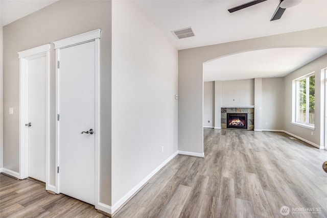 unfurnished living room with visible vents, baseboards, light wood-style flooring, a fireplace, and arched walkways