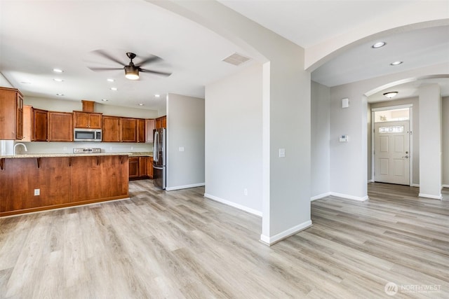 kitchen with light wood-type flooring, brown cabinets, a peninsula, appliances with stainless steel finishes, and a breakfast bar area