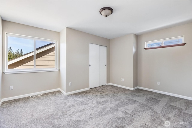 unfurnished bedroom with baseboards, multiple windows, carpet floors, and visible vents