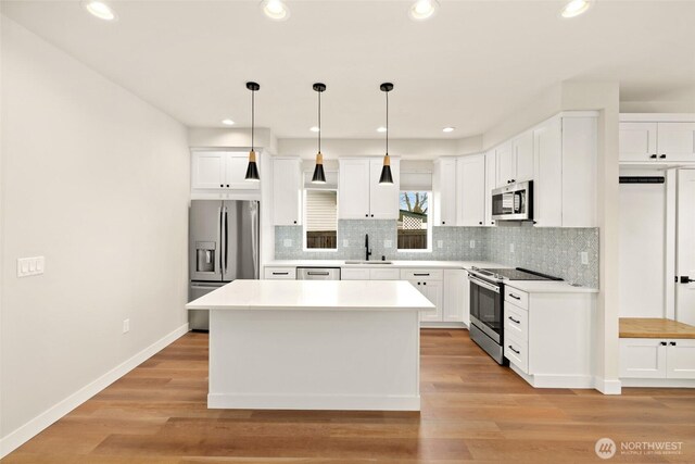 kitchen with light wood-style flooring, a sink, backsplash, stainless steel appliances, and white cabinets