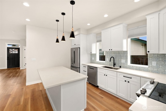 kitchen featuring a kitchen island, light wood-style flooring, a sink, appliances with stainless steel finishes, and white cabinetry