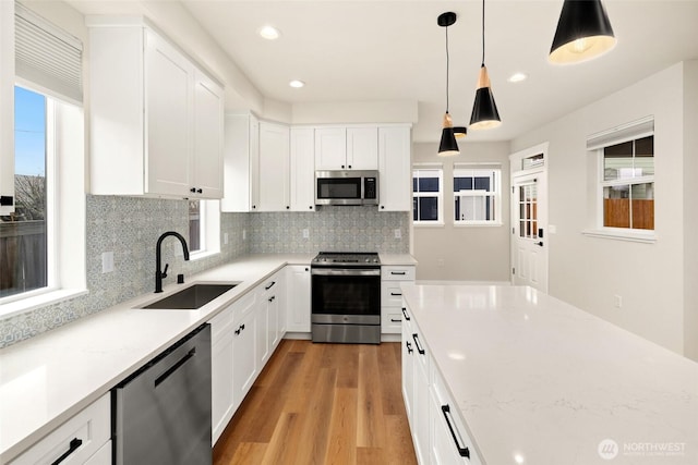 kitchen featuring a sink, stainless steel appliances, white cabinets, light wood-type flooring, and backsplash