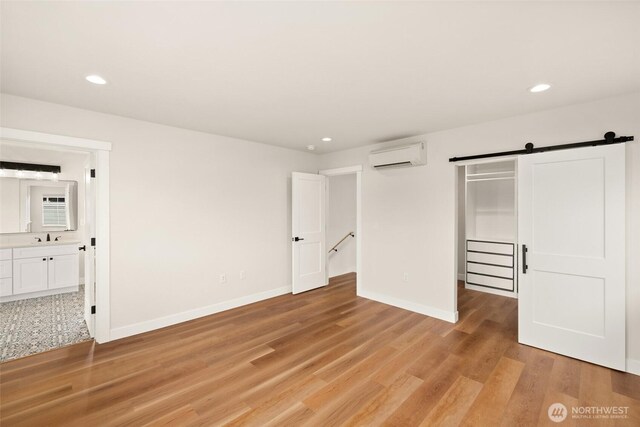 unfurnished bedroom with an AC wall unit, a barn door, light wood-style floors, and baseboards