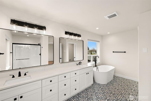 bathroom featuring double vanity, a freestanding tub, visible vents, and a sink