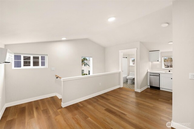 interior space featuring dishwasher, vaulted ceiling, wood finished floors, and white cabinetry