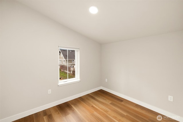 empty room featuring baseboards, wood finished floors, and vaulted ceiling