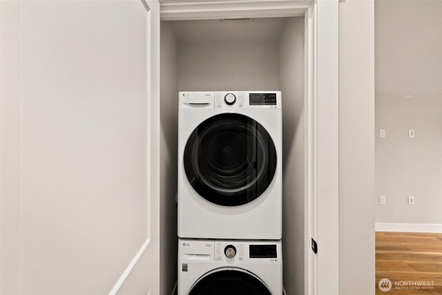 washroom featuring laundry area, stacked washing maching and dryer, baseboards, and wood finished floors