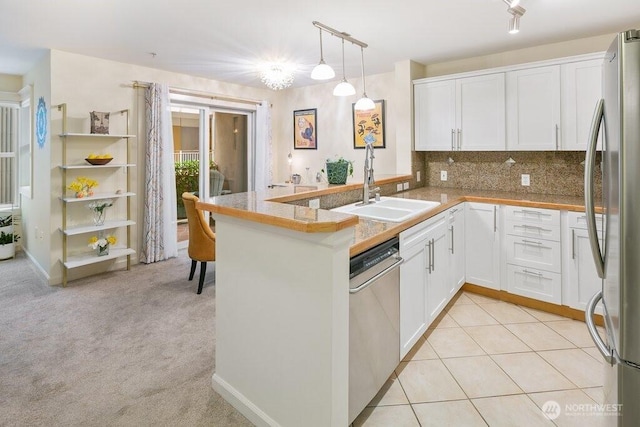 kitchen with light carpet, appliances with stainless steel finishes, a peninsula, white cabinetry, and a sink