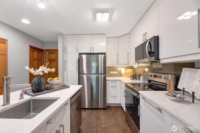 kitchen with dark wood-style flooring, a sink, decorative backsplash, stainless steel appliances, and white cabinetry