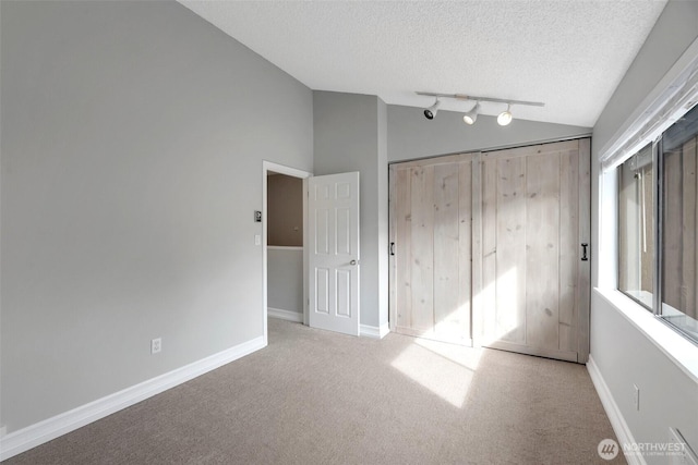 unfurnished bedroom with vaulted ceiling, carpet flooring, baseboards, and a textured ceiling