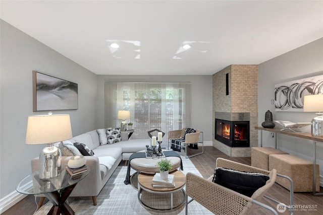 living area featuring baseboards, a large fireplace, and wood finished floors