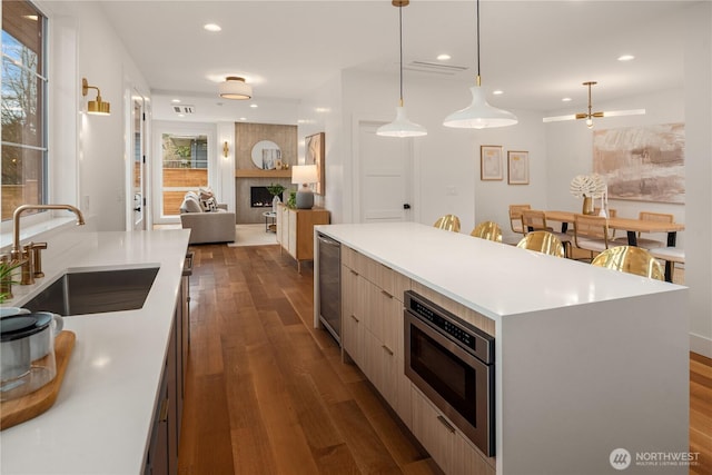 kitchen featuring stainless steel microwave, a sink, light countertops, modern cabinets, and dark wood-style flooring