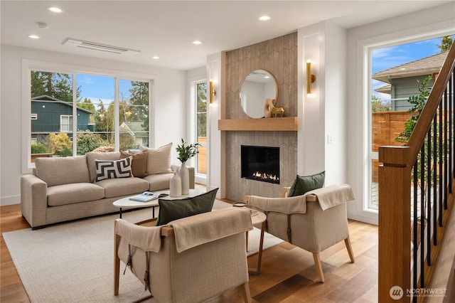 living room featuring a large fireplace, recessed lighting, light wood-type flooring, and visible vents